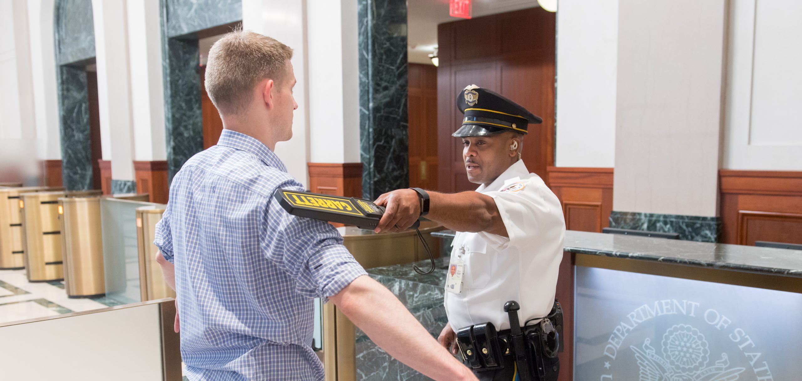 Security guard screens man with metal detector in lobby of department of state building